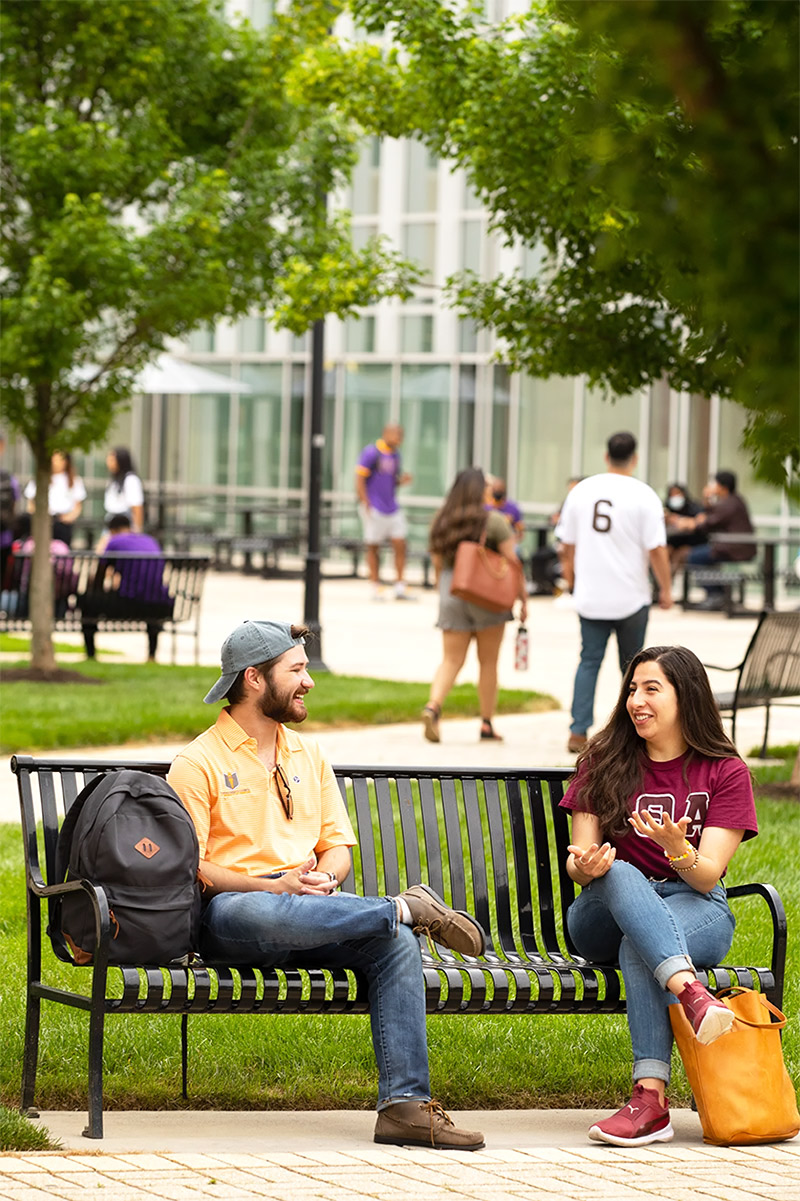 students sit on a bench in the middle of campus