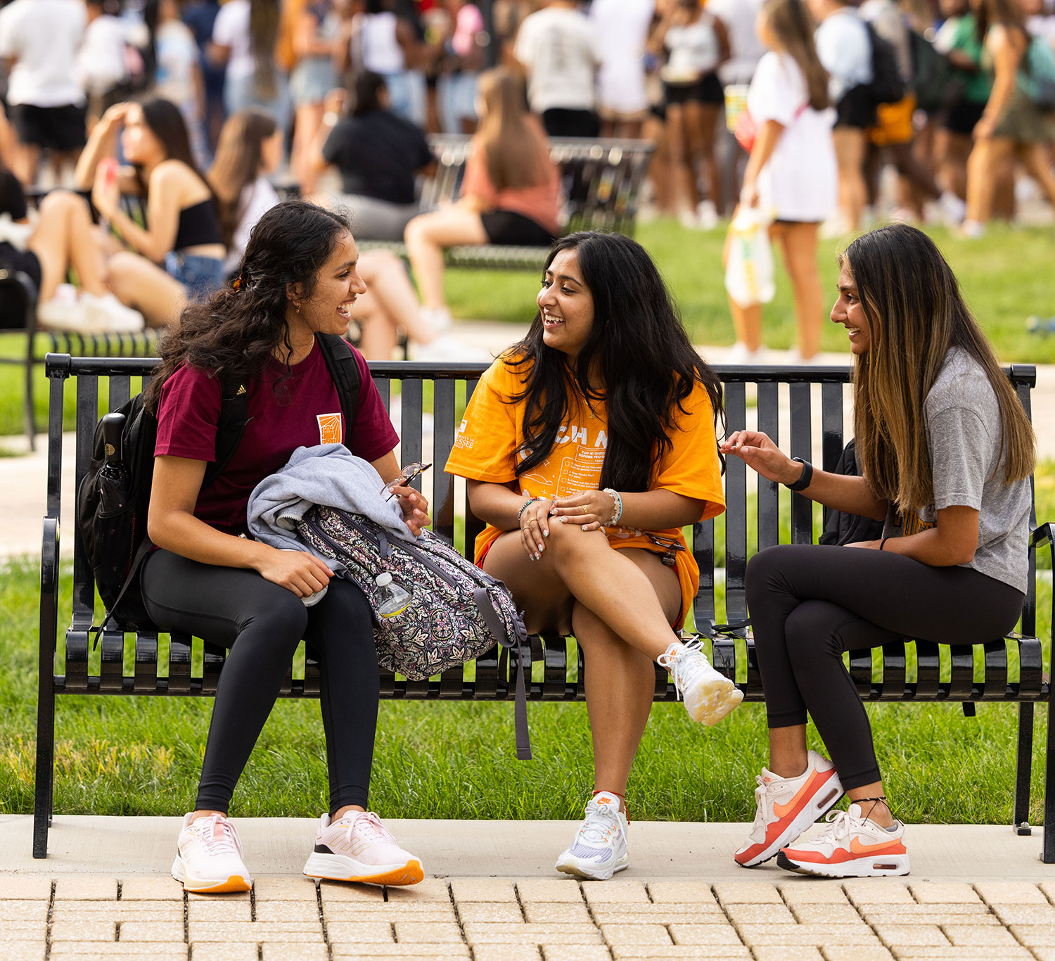 Three students hang out while sitting on a bench in the middle of UT' bustling campus.